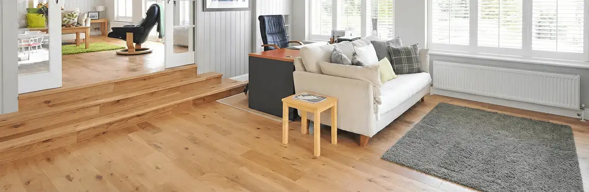 A modern living room with professionally installed laminate flooring, a beige sofa, a small side table, a gray rug, and large windows with white shutters in Ogden, UT